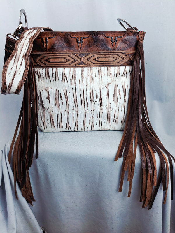 Brown leather handbag with white pattern and fringes on a light gray background