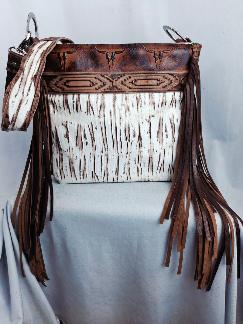 Brown leather handbag with white pattern and fringes on a light gray background